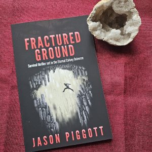Fractured Ground book on a red table runner & a crystal