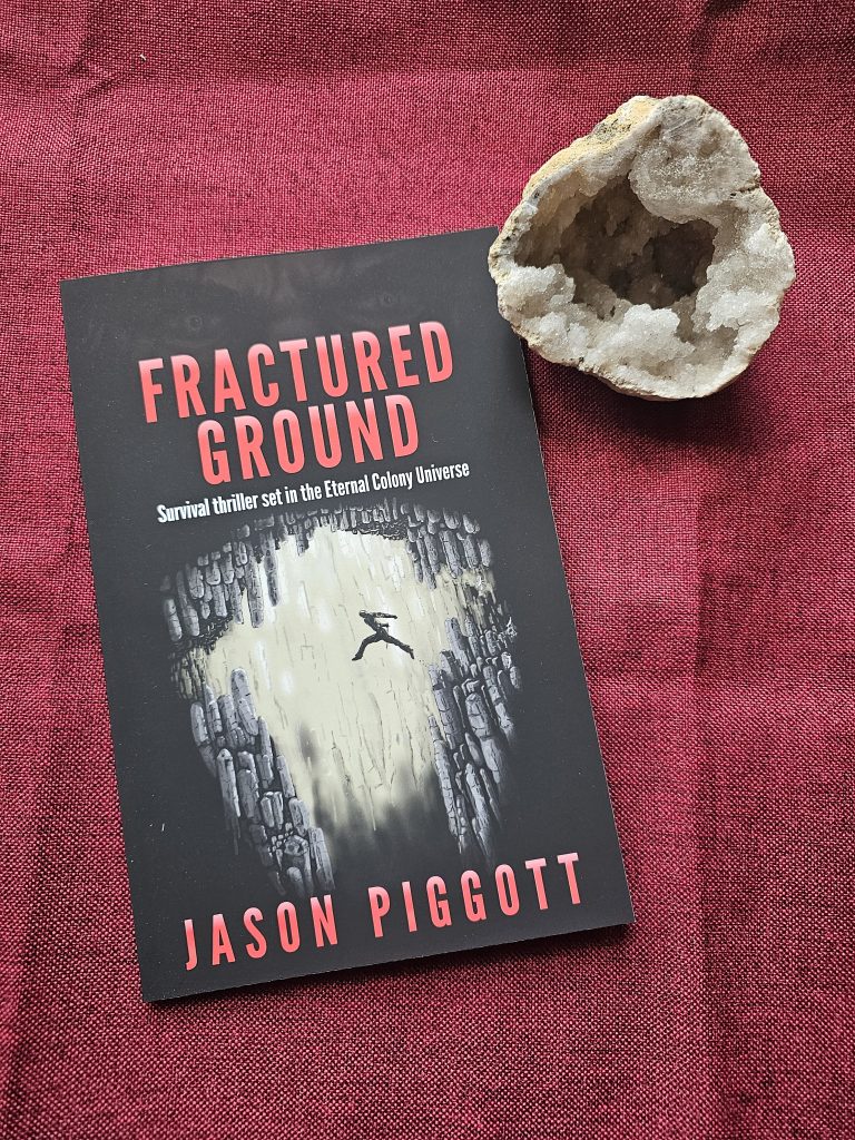 Fractured Ground book on a red table runner & a crystal