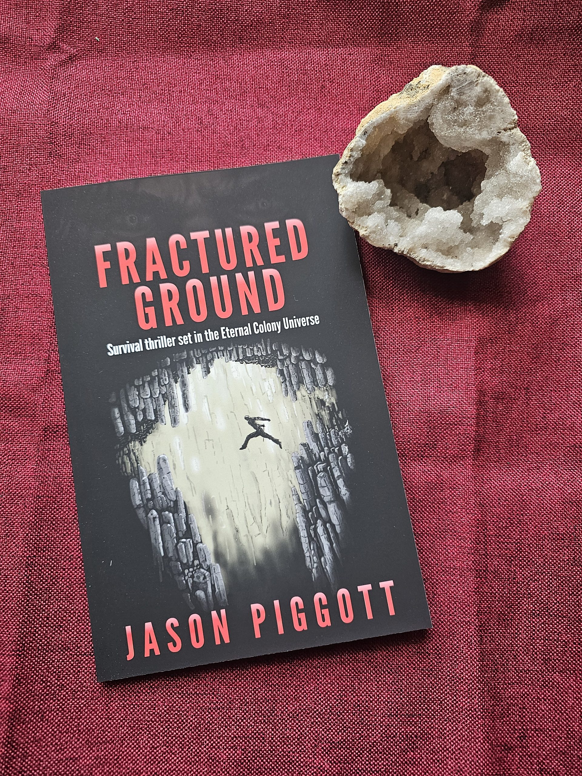 Fractured Ground book on a red table runner & a crystal